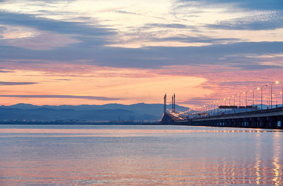 Illuminated bridge over lake against cloudy sky during sunset