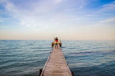 Rear view of man on jetty at sea against sky