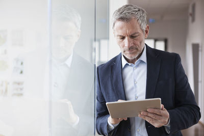 Successful businessman standing in his office holding digital tablet