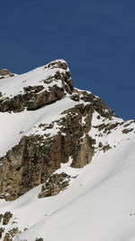 Low angle view of snowcapped mountains against clear blue sky