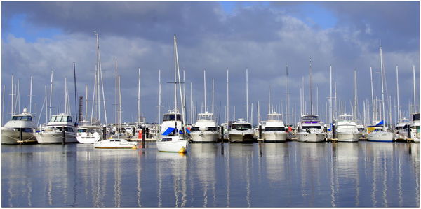 Boats moored in calm sea against cloudy sky