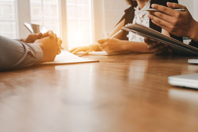 Midsection of people holding smart phone on table