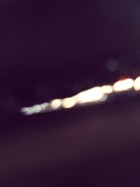 Defocused image of illuminated lights against sky at night