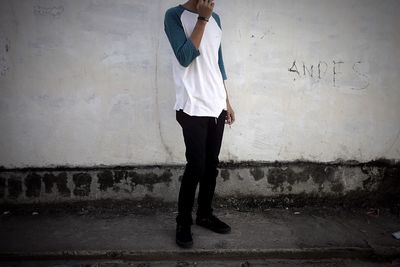 Low section of man holding cigarette against wall