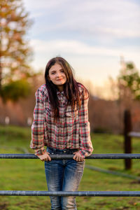 Portrait of young woman standing on metal gate