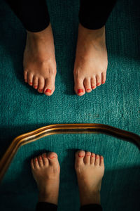 Feet with red painted toenails on teal carpet and gold rim mirror
