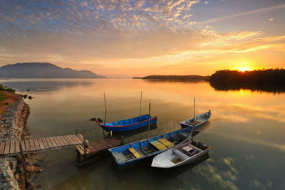 Boats in calm lake against sky during sunset