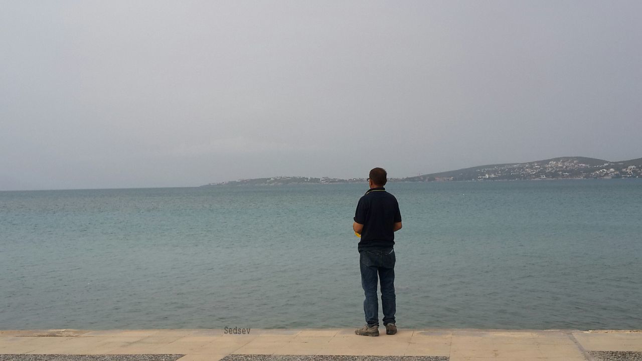 sea, water, rear view, standing, lifestyles, beach, leisure activity, tranquil scene, full length, tranquility, scenics, horizon over water, copy space, shore, beauty in nature, nature, clear sky, casual clothing