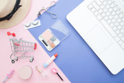 Directly above shot of shopping cart with cosmetics and laptop on table