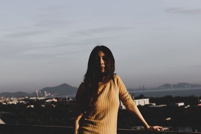 Young woman looking at cityscape against sky