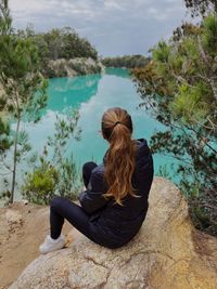 Rear view of woman sitting on rock by lake