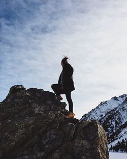 Low angle view of woman standing on rock formation against sky