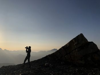 Man photographing on rock against sky