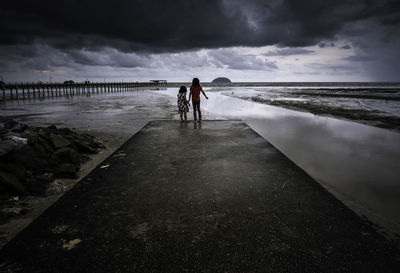 Rear view of sisters standing at beach against sky