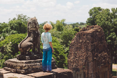 Side view of boy standing by statue against trees