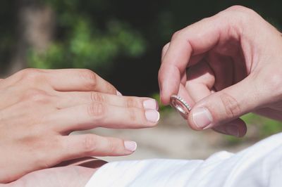 Cropped image of man putting ring in hand of woman