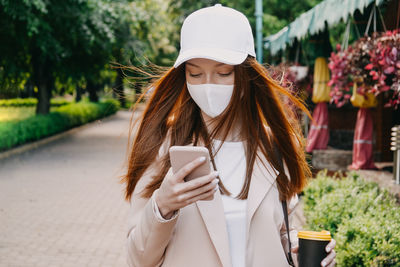 Redhead woman wearing face mask for virus protection. young business woman with cell phone in hand