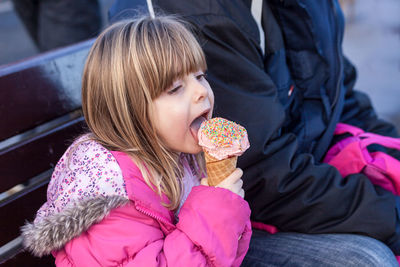 High angle view of girl licking ice cream while sitting with father on bench