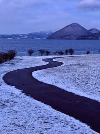 Scenic view of sea by mountains against sky during winter
