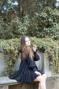 Young woman sitting on plant against trees