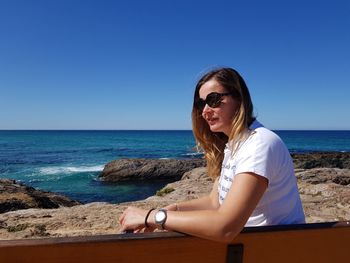 Young woman wearing sunglasses on beach against clear sky