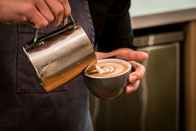 Midsection of man pouring milk in coffee cup