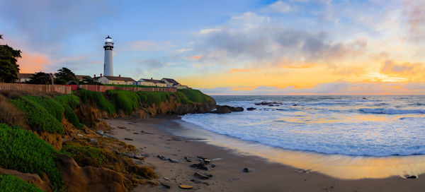 Lighthouse by sea against sky during sunset