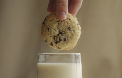 Close-up of hand holding cookies over milk