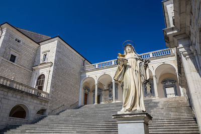 Low angle view of statues against building against clear blue sky