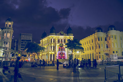 People at town square against illuminated buildings