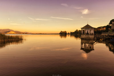 Scenic view of lake by building against sky during sunset