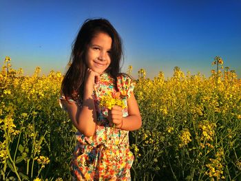 Portrait of smiling girl standing at oilseed rape field against sky