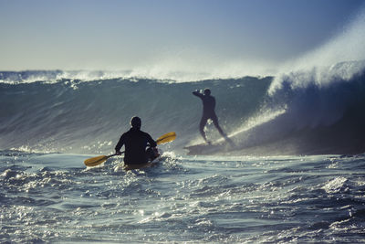 Friends surfboarding in sea against clear sky