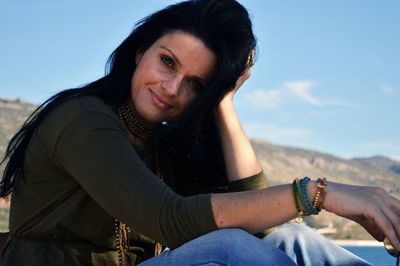 Portrait of beautiful woman with hand in hair against sky