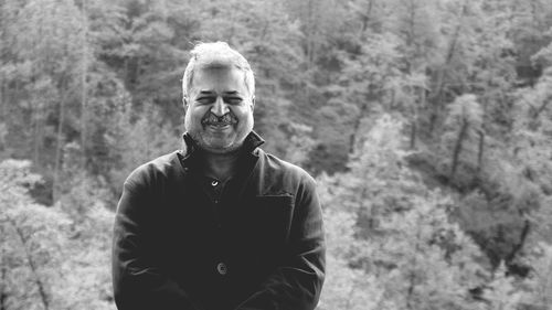 Portrait of man smiling while standing against trees