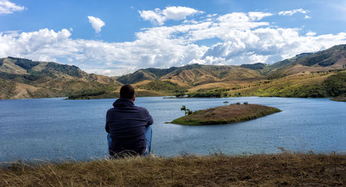 Rear view of man looking at lake against mountains