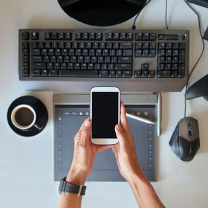 Midsection of person using mobile phone over desk workspace