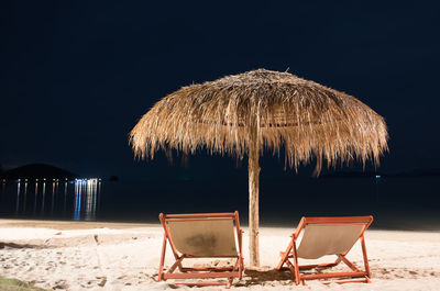 Lounge chairs and thatched roof at beach against sky