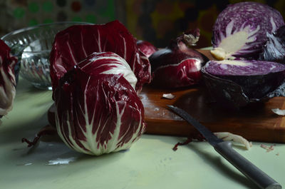  red radicchio, knife, cut red cabbage, red onion, on bamboo cutting board on light green surface