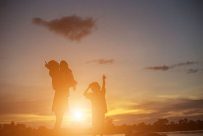 Silhouette friends standing against sky during sunset