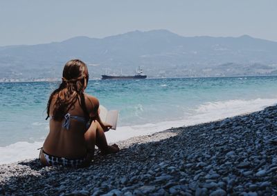 Rear view of woman sitting on beach against sky