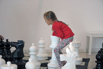 Side view of girl standing on artificial chess board at home