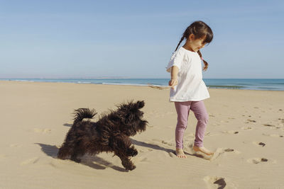 Side view of little girl walking with dog at beach