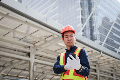 Architect using mobile phone while standing against buildings in city