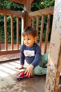 Boy playing with toy car while sitting by railing