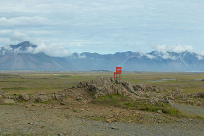 Scenic view of a single red chair with landscape against sky