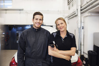 Portrait of happy mechanic standing with female in auto repair shop