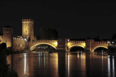 Illuminated castel vecchio bridge over river against sky at night