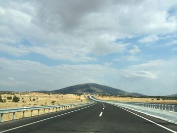 Road passing through landscape against cloudy sky