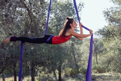 Young girl acrobat. practicing aerial silks. woman doing stunts with clothes in the forest. horizontal position.